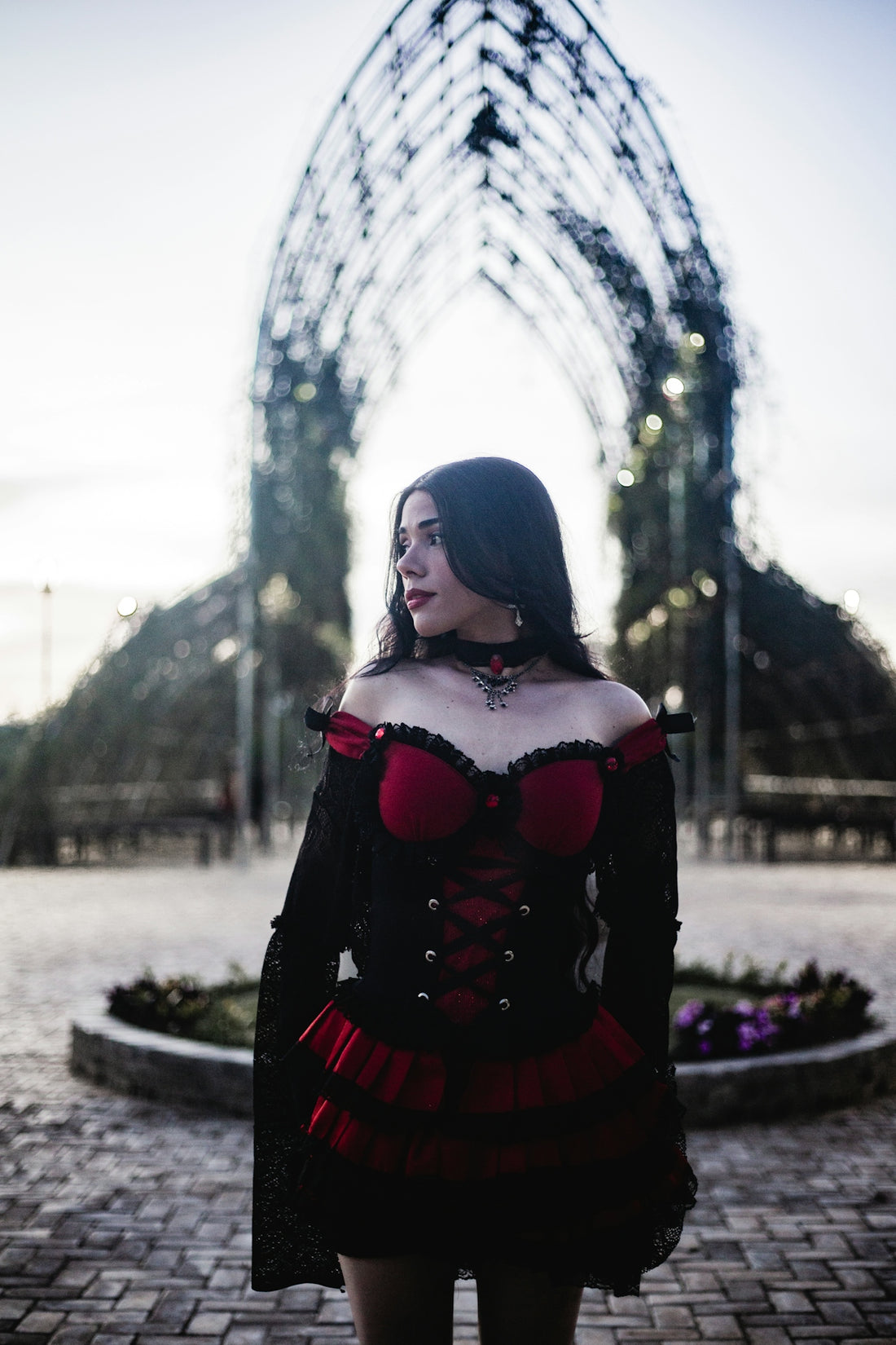 Woman in gothic dress stands outdoors near archway