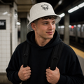 Man wearing white ALTRD bucket hat with logo, black hoodie, and backpack at subway station