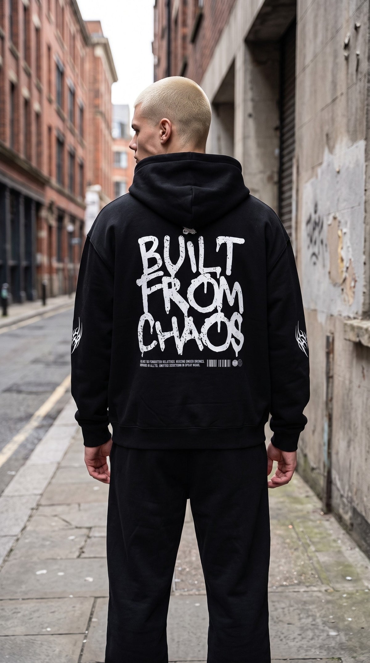 ALTRD Apparel black oversized fleece hoodie with white Built From Chaos graphic on back, worn by a man in an alley.